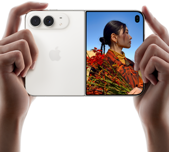 iPhone Duo, warna Putih Star White, dipegang dengan dua tangan dalam orientasi horizontal, tidak dilipat, panel kiri menampilkan kamera belakang Dual Fusion 48 MP, panel kanan menampilkan seseorang yang sedang difoto di layar luar, subjek foto dapat melihat wajahnya saat difoto menggunakan Duo Preview