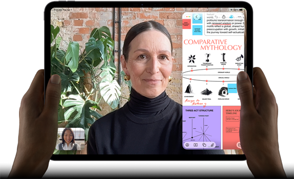 iPad Pro, eksterior depan, orientasi lanskap, warna hitam angkasa, sudut melengkung, bezel layar hitam, tangan memegang sisi kiri dan kanan, layar menampilkan percakapan FaceTime yang sedang diterjemahkan secara langsung, dan aplikasi pendidikan yang menampilkan presentasi "Mitologi Perbandingan" dengan teks, diagram, dan catatan tulisan tangan