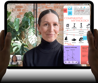 iPad Pro, eksterior depan, orientasi lanskap, warna hitam angkasa, sudut melengkung, bezel layar hitam, tangan memegang sisi kiri dan kanan, layar menampilkan percakapan FaceTime yang sedang diterjemahkan secara langsung, dan aplikasi pendidikan yang menampilkan presentasi "Mitologi Perbandingan" dengan teks, diagram, dan catatan tulisan tangan